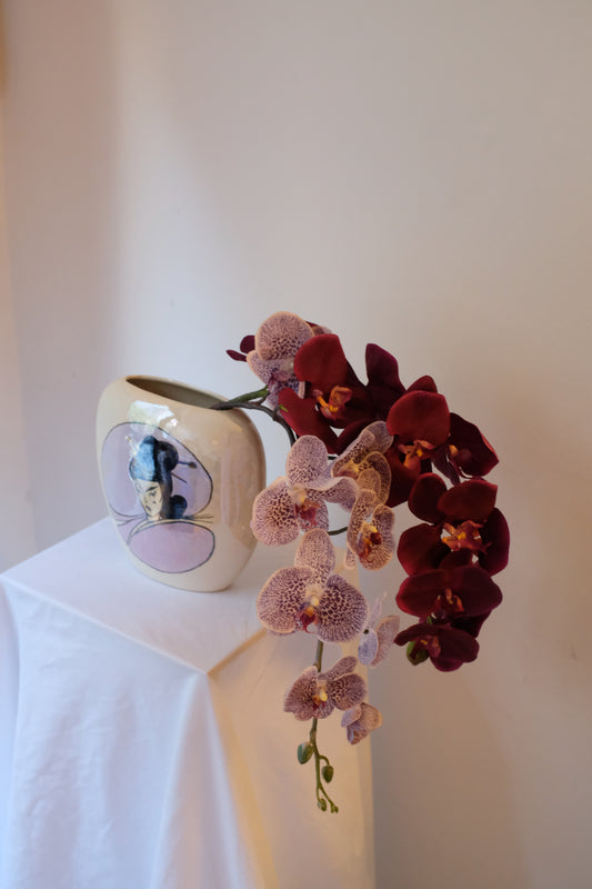 Burgundy Orchids — silk burgundy phalaenopsis and spotted vanda orchids in a pearl-glazed ceramic vintage vessel with geisha portrait.