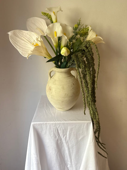 The Local — silk white anthuriums, calla lilies, and Easter lilies with trailing green amaranthus in a vintage cream stone urn. Made to order in NYC.