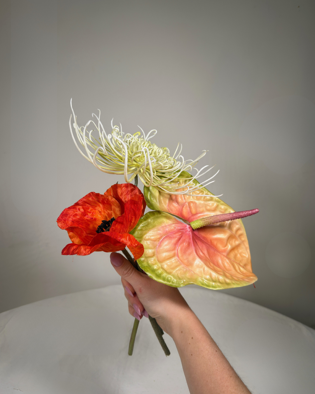 Hand holding the Henry St Mini silk flower bouquet — close-up of real-touch red poppy, copper anthurium, and spider mum stems. Handmade in NYC.
