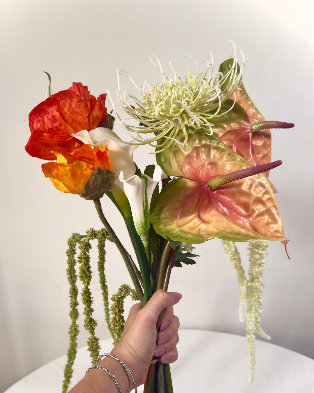 Hand holding The Henry St Large silk flower bouquet — close-up of real-touch orange anthurium, copper rose, calla lily, and spider mum stems. NYC made to order.