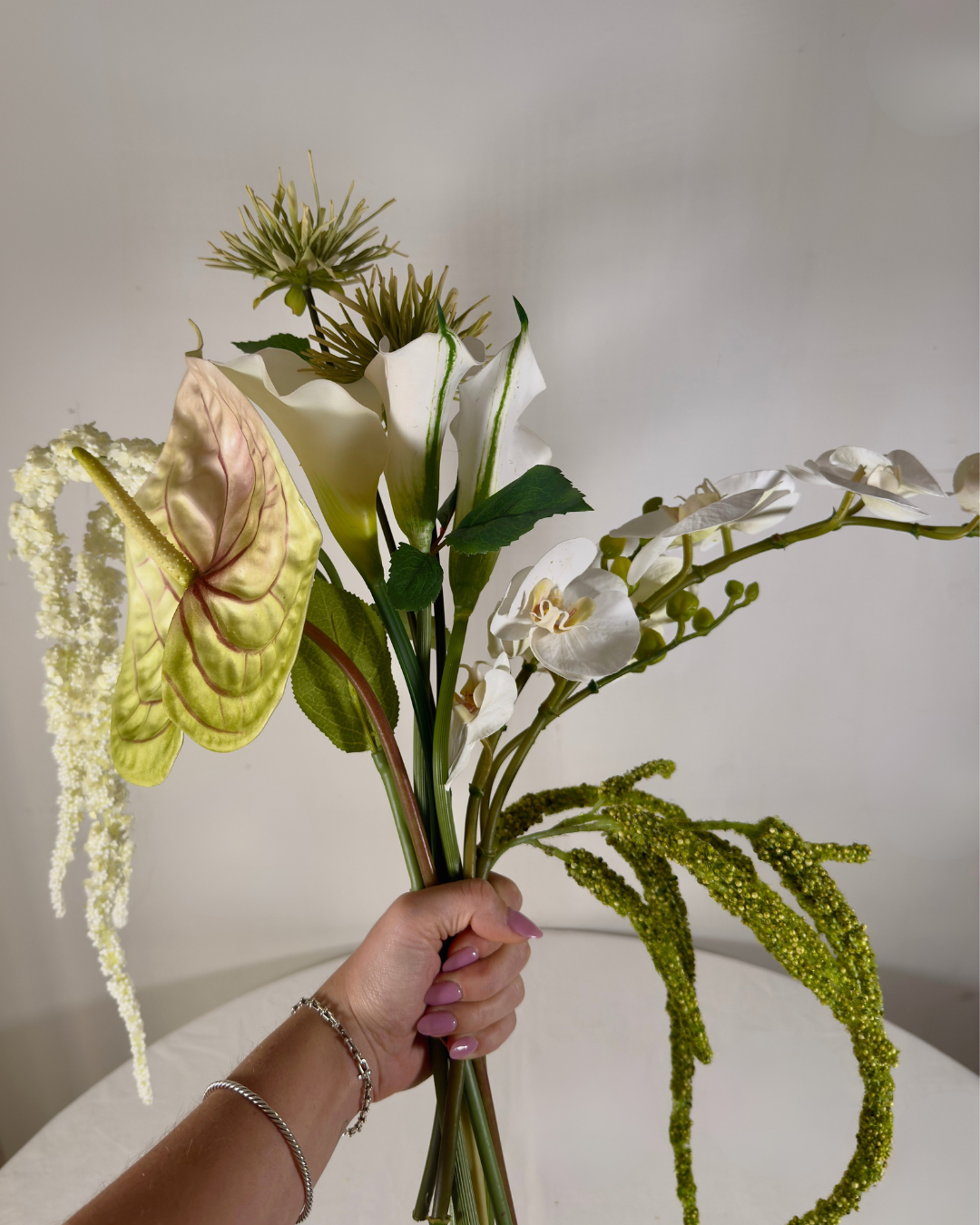 Hand holding The Sara J Large silk bouquet showing white orchid, anthurium, and calla lily stems.